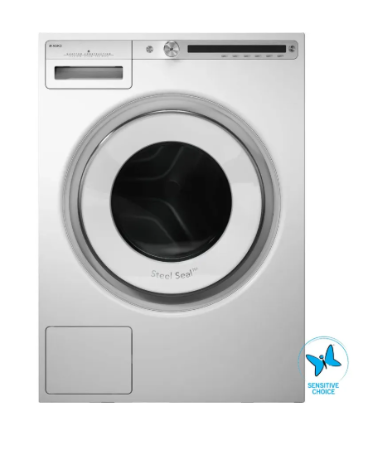 A front-loading washing machine in a brushed silver finish, featuring a large circular door with a black interior, a control panel at the top, and a Steel Seal badge on the door. A blue and white Sensitive Choice logo is visible in the bottom right corner.